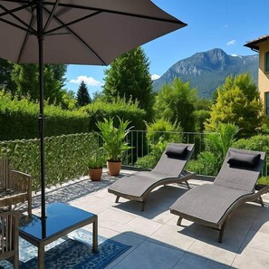 Une terrasse avec deux chaises longues, une table et un parasol.