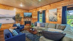 Ein gemütliches Blockhaus-Interieur mit Kamin, einer Couch, einem Couchtisch und einem Fernseher.