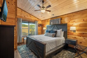 A wooden-paneled bedroom with a bed, bedside lamps, a ceiling fan, and a window with curtains. - Great location, Pigeon Forge: 5 bedroom with theatre, game room, hottub (Pigeon Forge)
