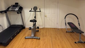Ein Heimfitnessraum mit Laufband, Hometrainer und einer Bank.