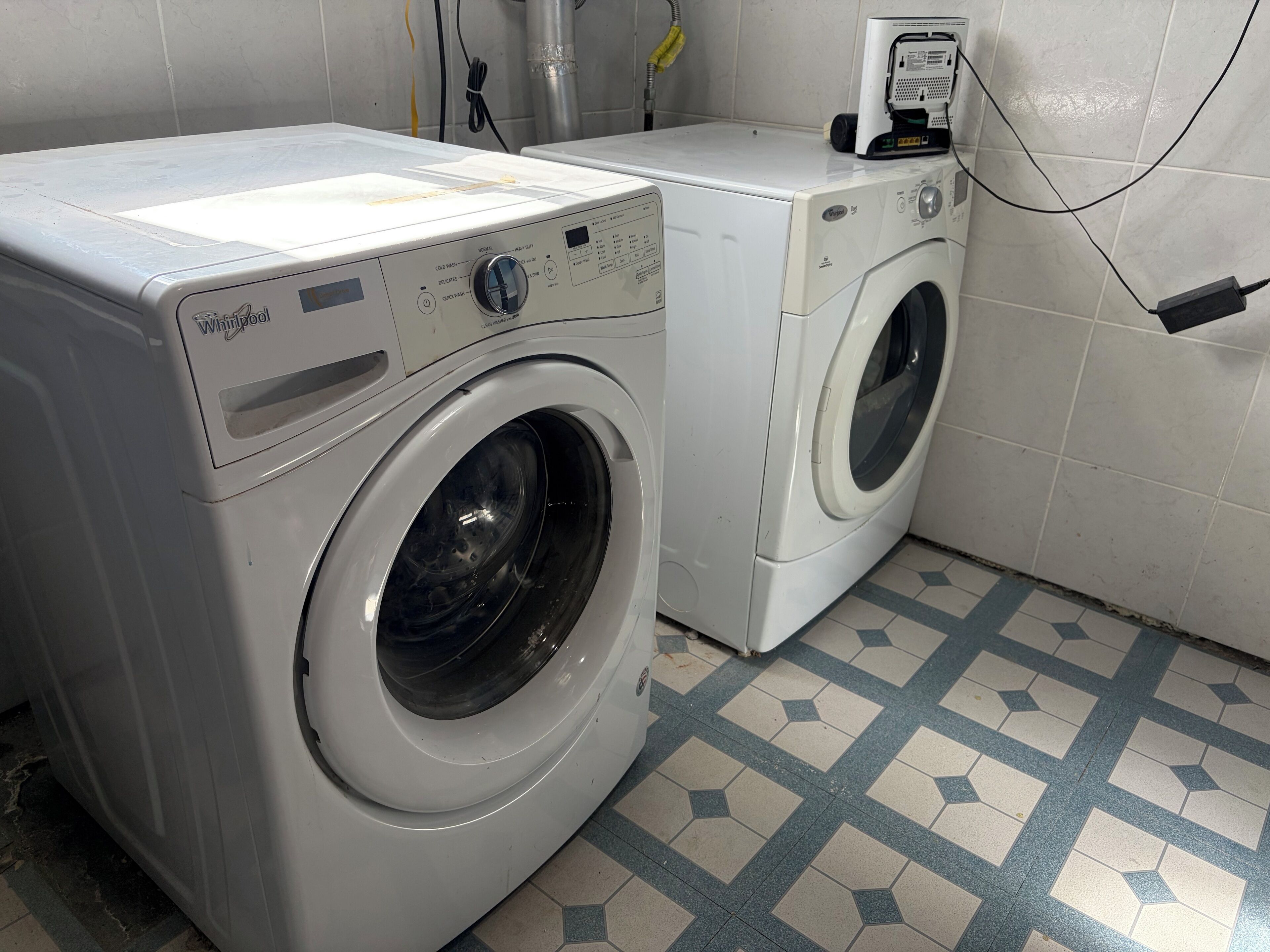A front-loading Whirlpool washer and dryer in a laundry room with a tiled floor.