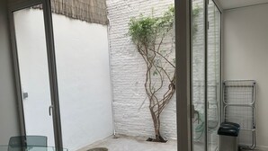 A small, enclosed outdoor area with a concrete floor, a glass door, a metal rack, and a small tree. - Cozy house in the heart of Mataró (Mataró)