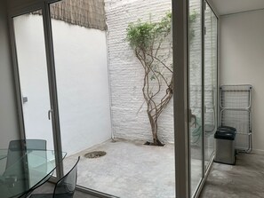 A small, enclosed outdoor area with a concrete floor, a glass door, a metal rack, and a small tree. - Cozy house in the heart of Mataró (Mataró)
