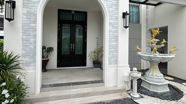 A modern building with a white facade, a black door, and a decorative fountain with golden statues. - House Near Suvarnabhumi Airport (Bangkok)