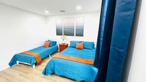Una stanza con due letti, ognuno con biancheria azzurra e cuscini arancioni, un comodino con una lampada e un'ampia finestra vista mare.