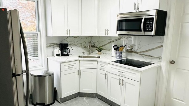 Una cucina moderna con mobili bianchi, un frigorifero in acciaio inox, un forno a microonde e un lavello.