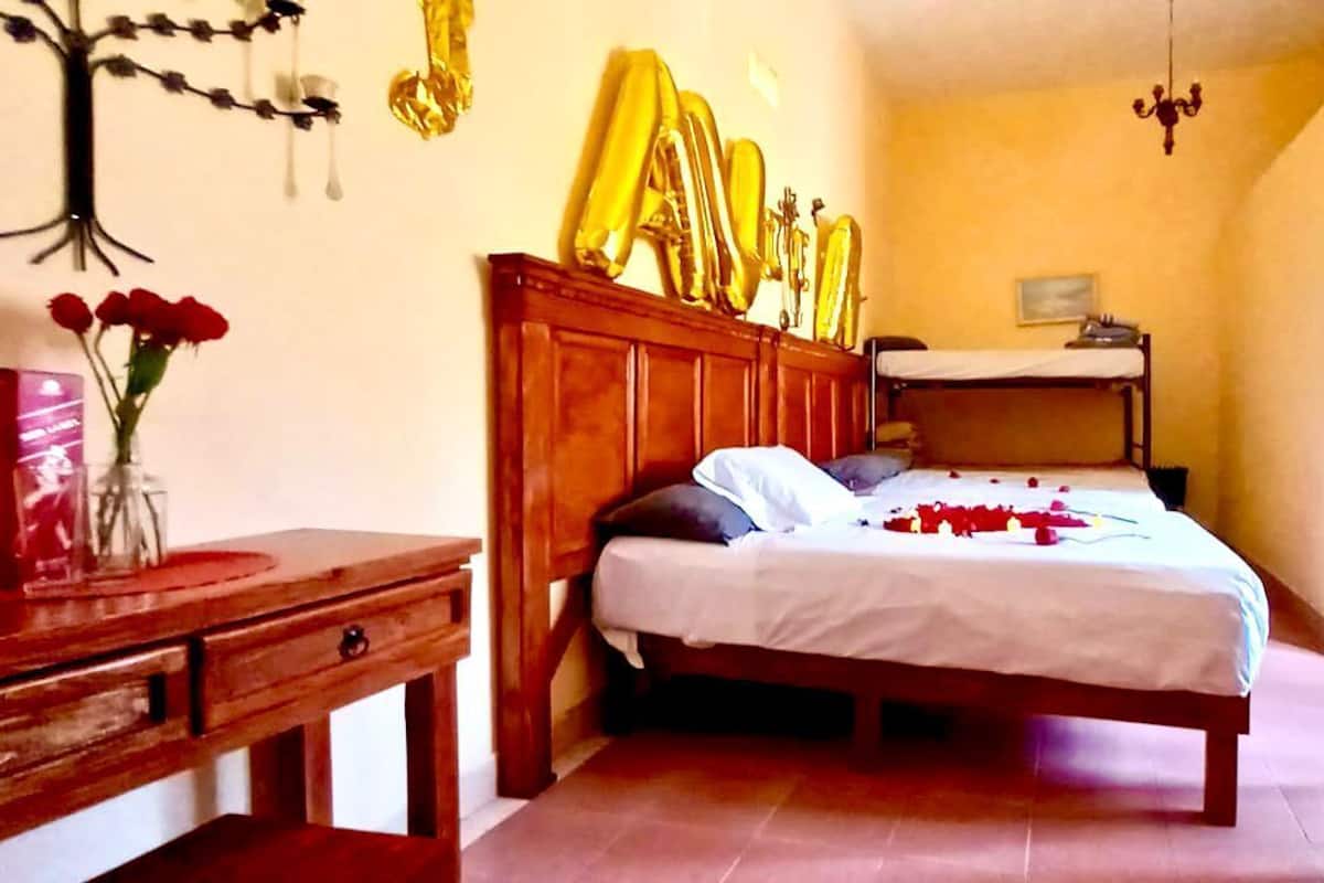 A bedroom with a wooden bed, a nightstand, a dresser, and a wall-mounted shelf with decorative items.