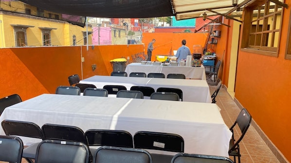 Un comedor con mesas preparadas para recibir a los comensales, asientos al aire libre y vistas de la ciudad.