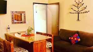 Een eethoek met een houten tafel en stoelen, een bank, een decoratieve boom en een spiegel aan de muur.