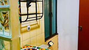 Een badkamer met een betegelde muur, een raam, een toilet en een wastafel met een vrolijk gekleurde spatwand.