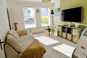 A living room with a sofa, a television, a bookshelf, and a window with blinds. - Spacious 4BR Home near Derry & Foyle Golf Club (Londonderry)