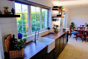 A kitchen with a window, a sink, a dining table with chairs, and a basket of items on the counter. - Spacious 4BR Home near Derry & Foyle Golf Club (Londonderry)