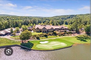 Un parcours de golf doté d’un club-house, entouré d’une zone boisée et bordé par un plan d’eau.