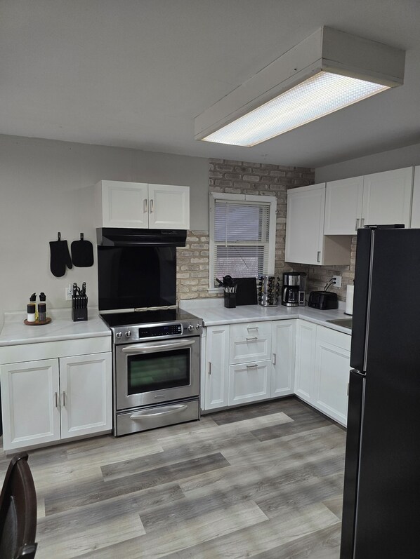 A modern kitchen with white cabinets, a stainless steel oven, a black range hood, and a built-in microwave.