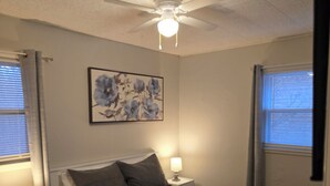 A bedroom with a bed, two bedside tables with lamps, a ceiling fan, and a wall-mounted painting.
