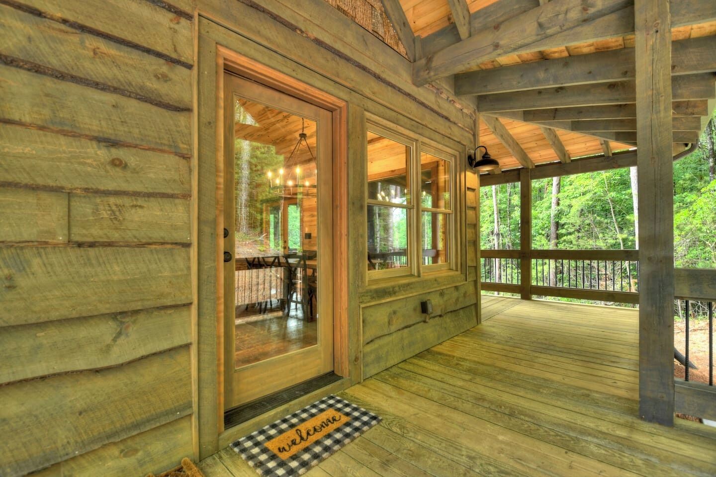 A wooden cabin with a porch, large windows, and a welcome mat.