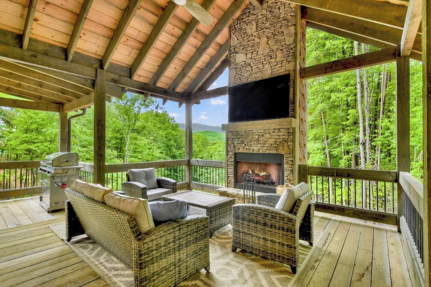 A covered outdoor area with wicker furniture, a stone fireplace, and a grill.