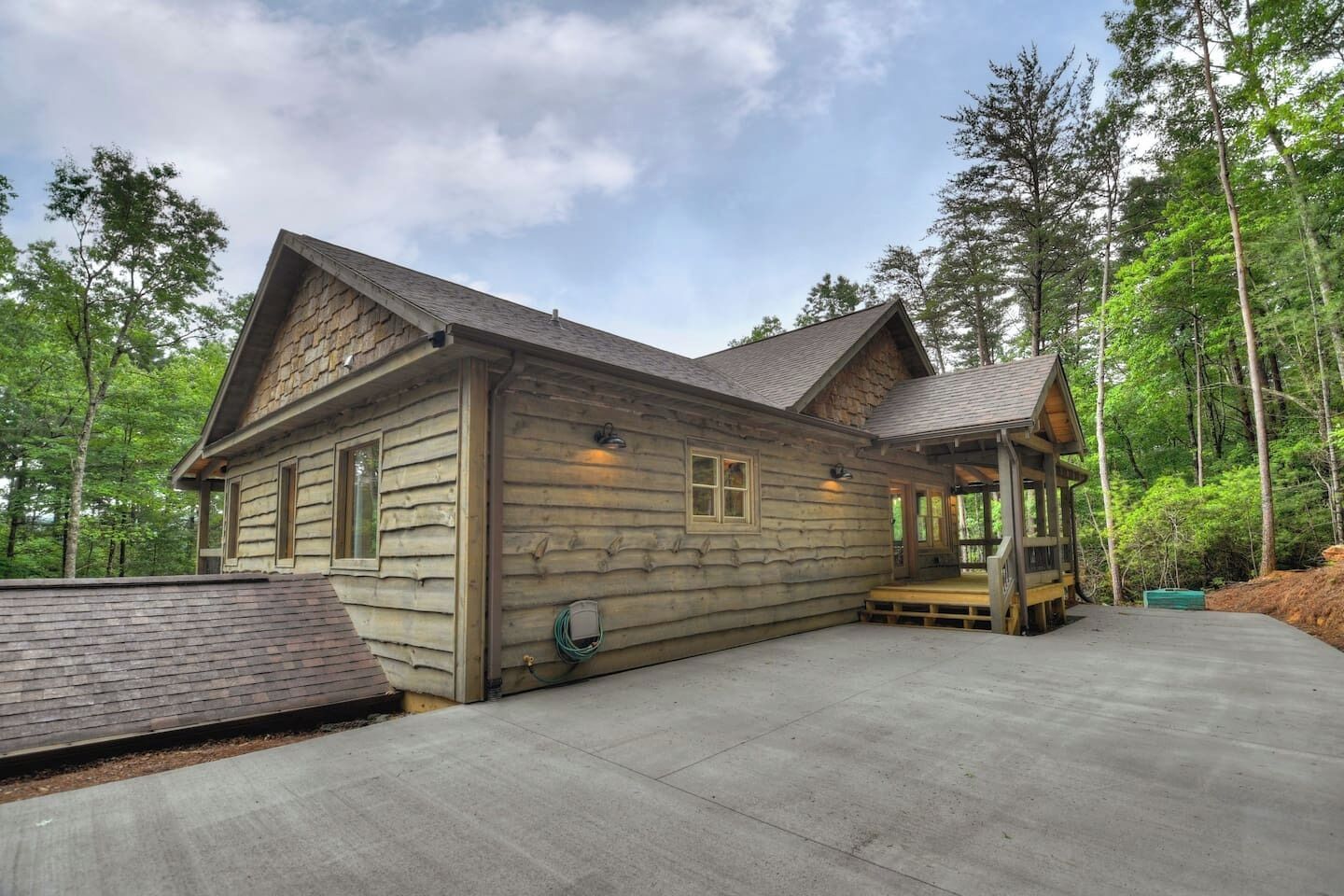 A log cabin with a covered porch and a concrete driveway.