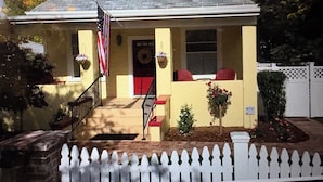 A yellow house with a red door, a flag, and a picket fence.