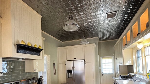 A modern kitchen with stainless steel appliances, wooden cabinets, and a patterned ceiling.