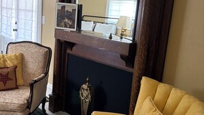 A living room with a fireplace, a mirror, a yellow armchair, a patterned armchair, and a plaid rug.