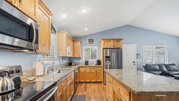 Una cocina con armarios de madera, electrodomésticos de acero inoxidable, encimeras de granito y un sofá de cuero negro en la sala.
