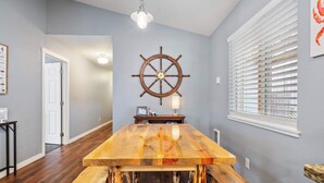 Un comedor con una mesa de madera, un adorno con timón de barco y una ventana con persianas.