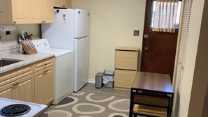 Cocina pequeña y funcional con estufa, pileta y electrodomésticos blancos. Un tapete estampado cubre el piso y una mesa de madera con sillas completa el espacio.
