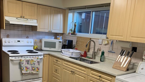 Una cocina con gabinetes de madera, una estufa blanca, un microondas y un fregadero.