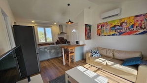 A modern living room with a TV, a sofa, a coffee table, and a kitchen area with a dining table. - Les Photinias Giens Peninsula Beach King-Size Bed (Hyères)
