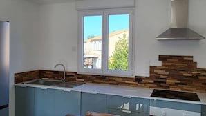 A modern kitchen with a central island, a built-in sink, and a window providing a view of the outside. - Les Photinias Giens Peninsula Beach King-Size Bed (Hyères)