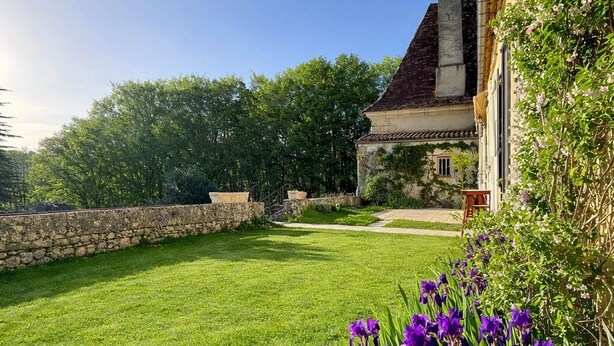 A well-maintained lawn with purple flowers in the foreground, a stone wall, and a building with a tiled roof. - La chartreuse de Caville, swimming pool & nature (Eyraud-Crempse-Maurens)