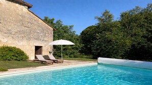A swimming pool with lounge chairs and an umbrella, surrounded by greenery and stone walls. - La chartreuse de Caville, swimming pool & nature (Eyraud-Crempse-Maurens)