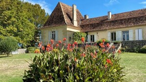A traditional building with a pitched roof and chimneys, surrounded by a well-maintained lawn and flowering plants. - La chartreuse de Caville, swimming pool & nature (Eyraud-Crempse-Maurens)