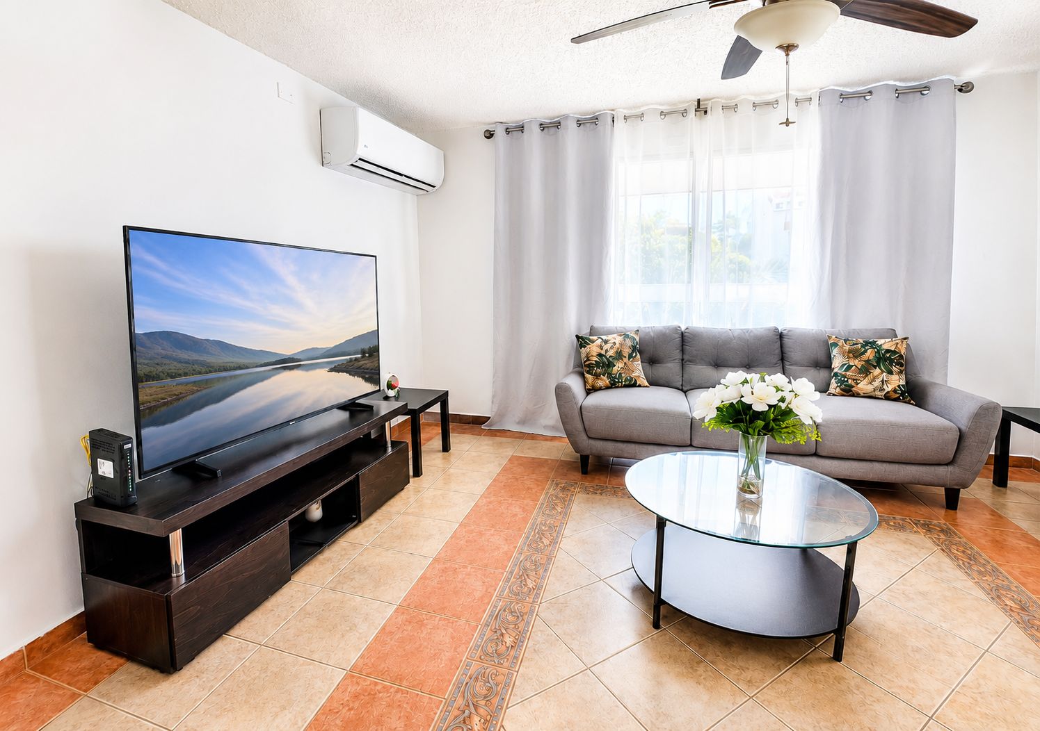 Ein Wohnzimmer mit Flachbildfernseher, einer Couch, einem Couchtisch und einem Deckenventilator.