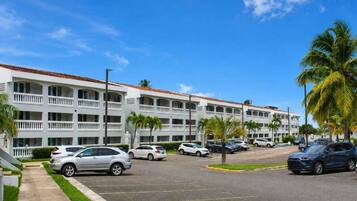 A multi-story hotel with a parking lot, palm trees, and a clear blue sky.