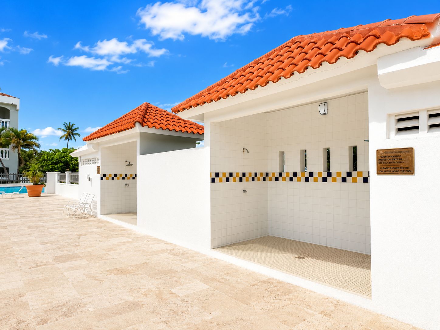 A poolside area with a tiled floor, a red-tiled roof, and a white building with a tiled wall.