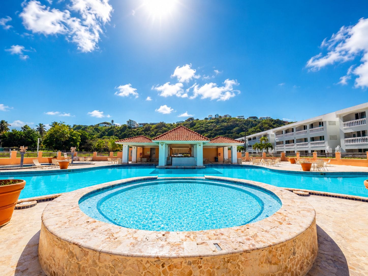 A swimming pool with a circular hot tub in the center, surrounded by lounge chairs and a covered seating area.