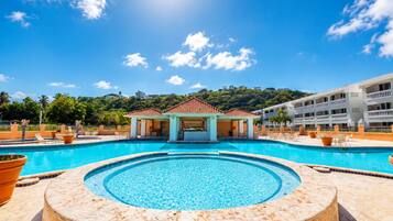 A swimming pool with a circular hot tub in the center, surrounded by lounge chairs and a covered seating area.