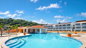 Un resort con una amplia piscina, varias construcciones con balcones y un paisaje montañoso al fondo.