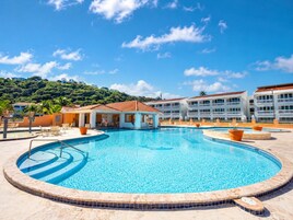 Un resort con una amplia piscina, varias construcciones con balcones y un paisaje montañoso al fondo.