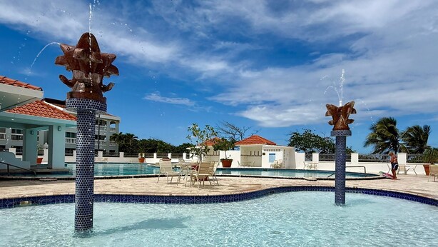 A pool area with two water fountains, lounge chairs, and a building with a tiled roof in the background. - Golden Dream Villa 2nd floor A (Isabela)