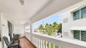 Een balkon met witte balustrades, uitzicht op palmbomen en een straat met geparkeerde auto's.