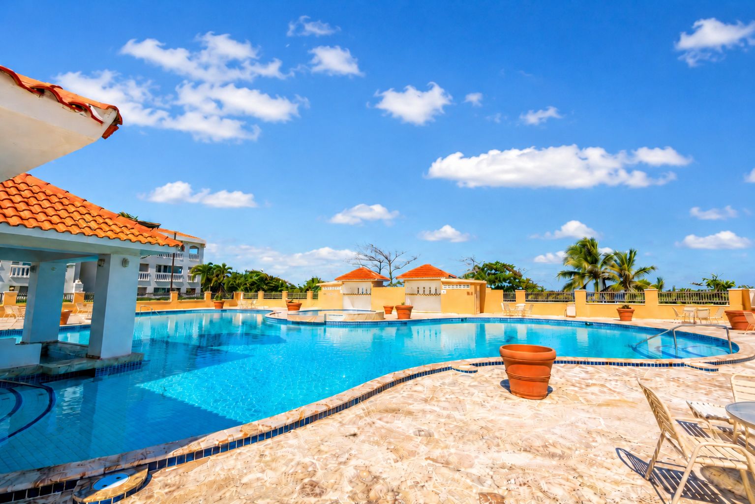 A swimming pool with a tiled edge, lounge chairs, and a clear blue sky.