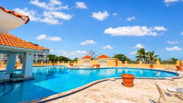 A swimming pool with a tiled edge, lounge chairs, and a clear blue sky.