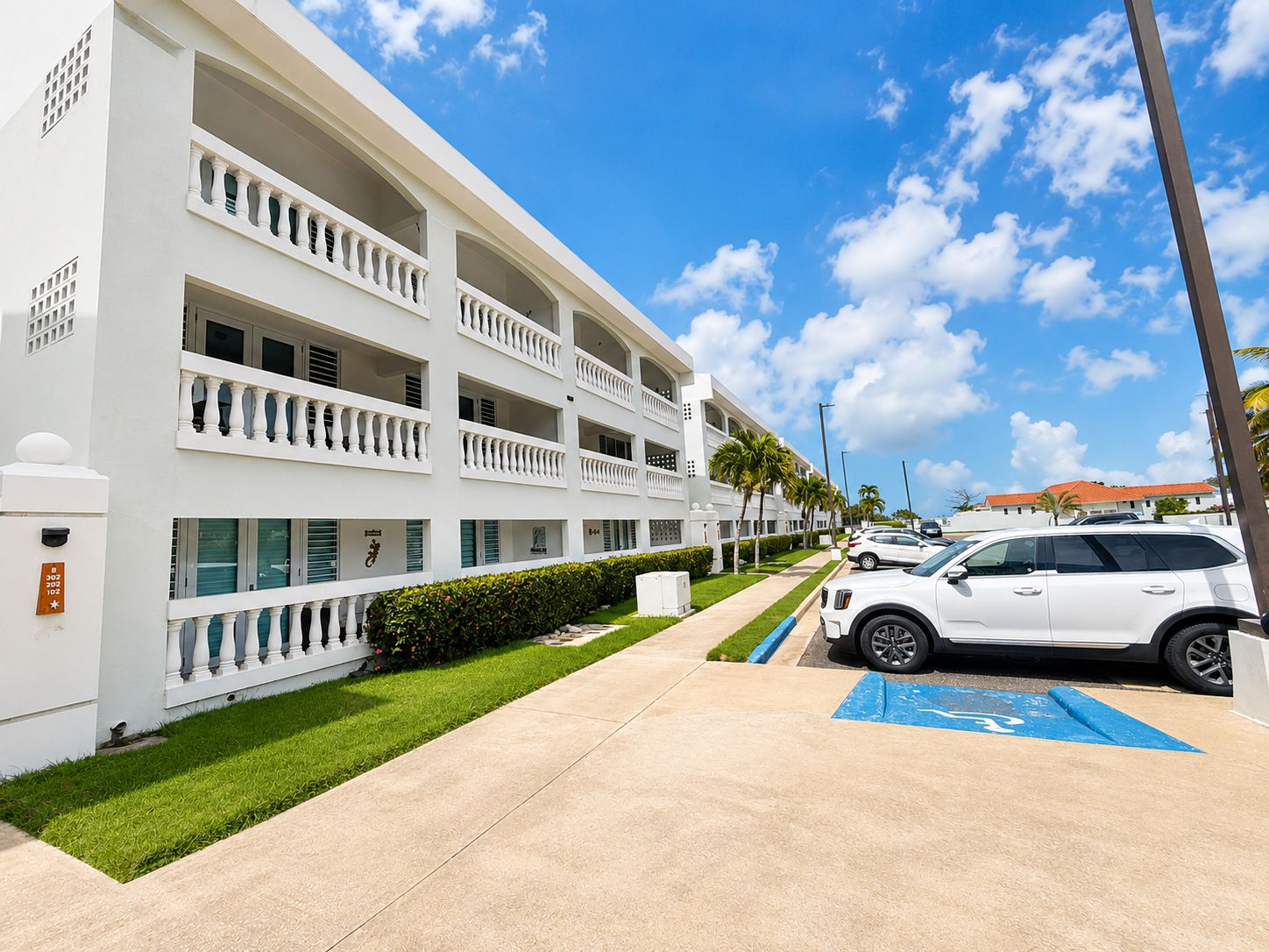 A multi-story hotel with a white exterior, a parking area with a blue handicapped parking space, and a clear blue sky.