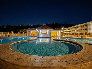 A swimming pool with a circular design, a covered seating area, and a building in the background. - Golden Dream Villa 2nd floor A (Isabela)