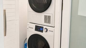 Une machine à laver et un sèche-linge superposés dans une buanderie, avec une porte blanche et un sol carrelé.