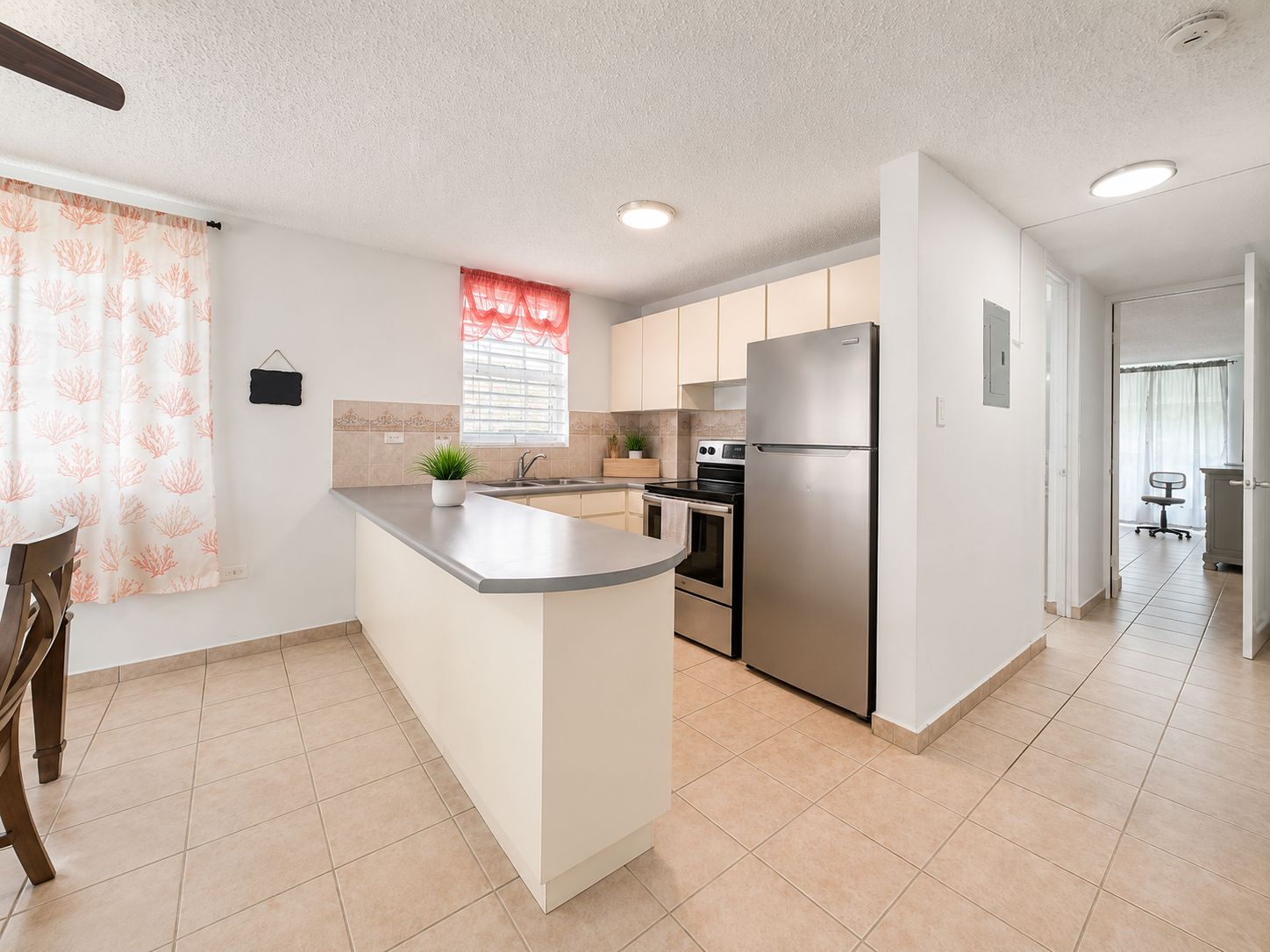 A modern kitchen with a central island, stainless steel appliances, and a window with a red curtain.