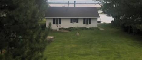 Ein Haus mit einem Rasen und einem Gewässer im Hintergrund.